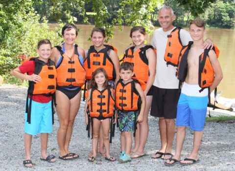 a family of rafters posing in lifejackets with the river in the background