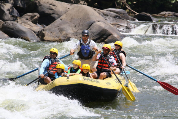a group including adults and kids approaching a whitewater rapid