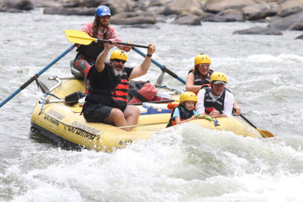 a family with a small child laughing as they approach a rapid in a raft