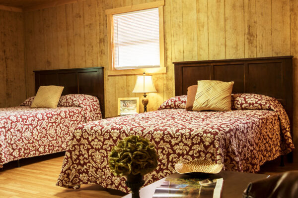 two beds inside a bungalow with a chair and table in frame