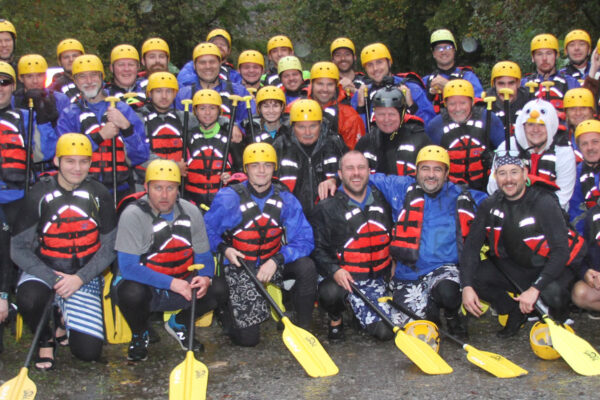 a group of rafters posing with their gear and paddles before hitting the water