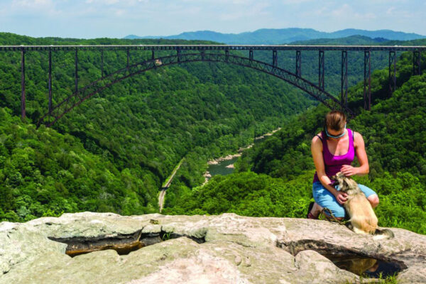 a woman and a dog posing on a rock in front of the famous bridge