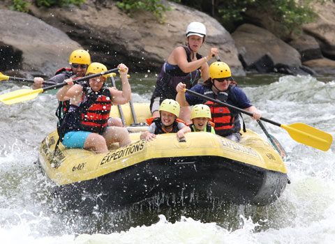 Two children sit in front of raft while adults and guide navigate the river at River Expeditions West Virginia