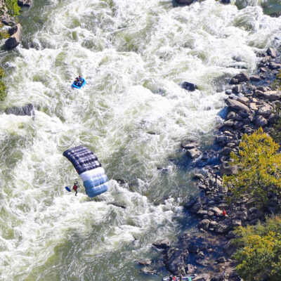 a parachuter over the whitewater rapid with a small raft going down the river