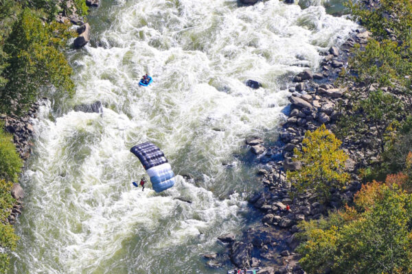 a parachuter over the whitewater rapid with a small raft going down the river